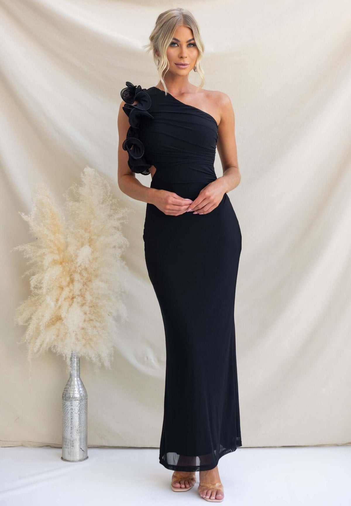 Model wearing a black one-shoulder maxi dress with floral detailing and a cut-out at the waist.