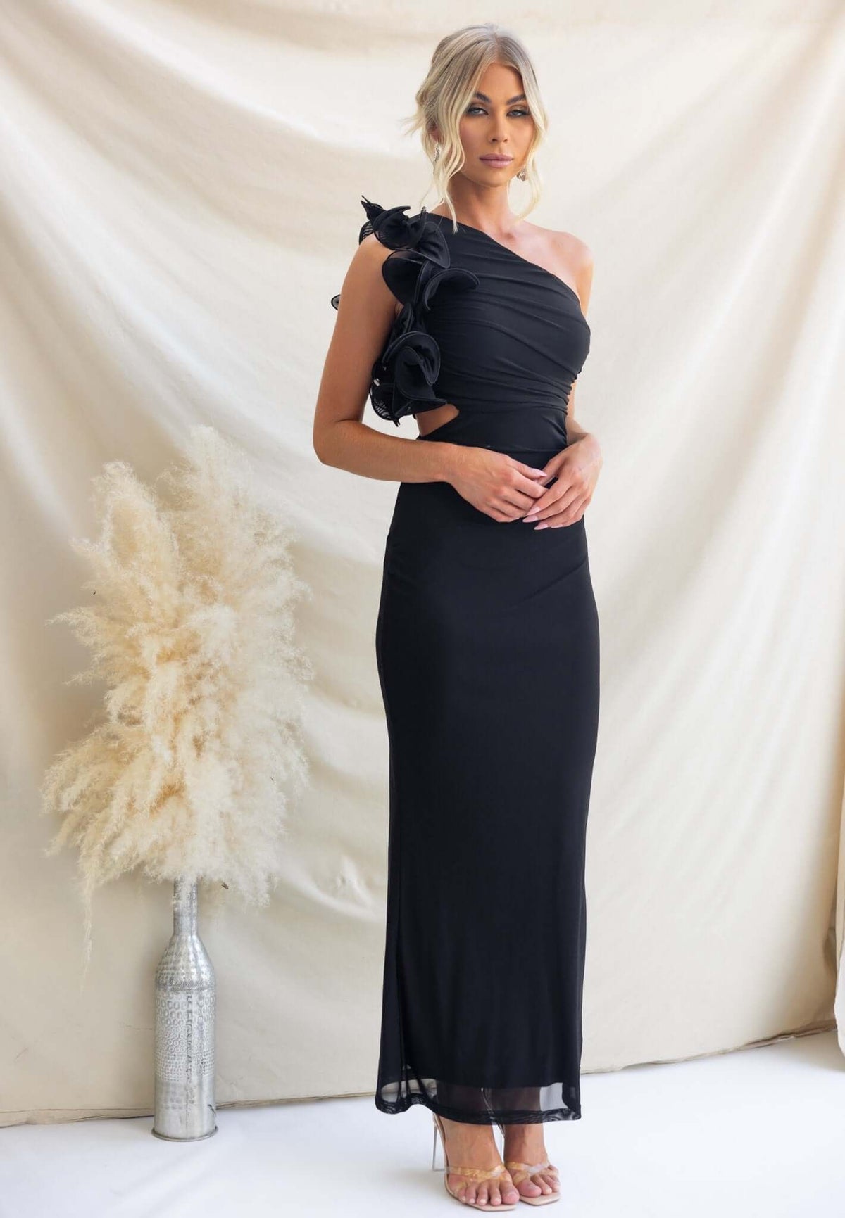 Model in black Meriden Maxi Dress with one-shoulder neckline and floral detail, styled against a neutral backdrop.