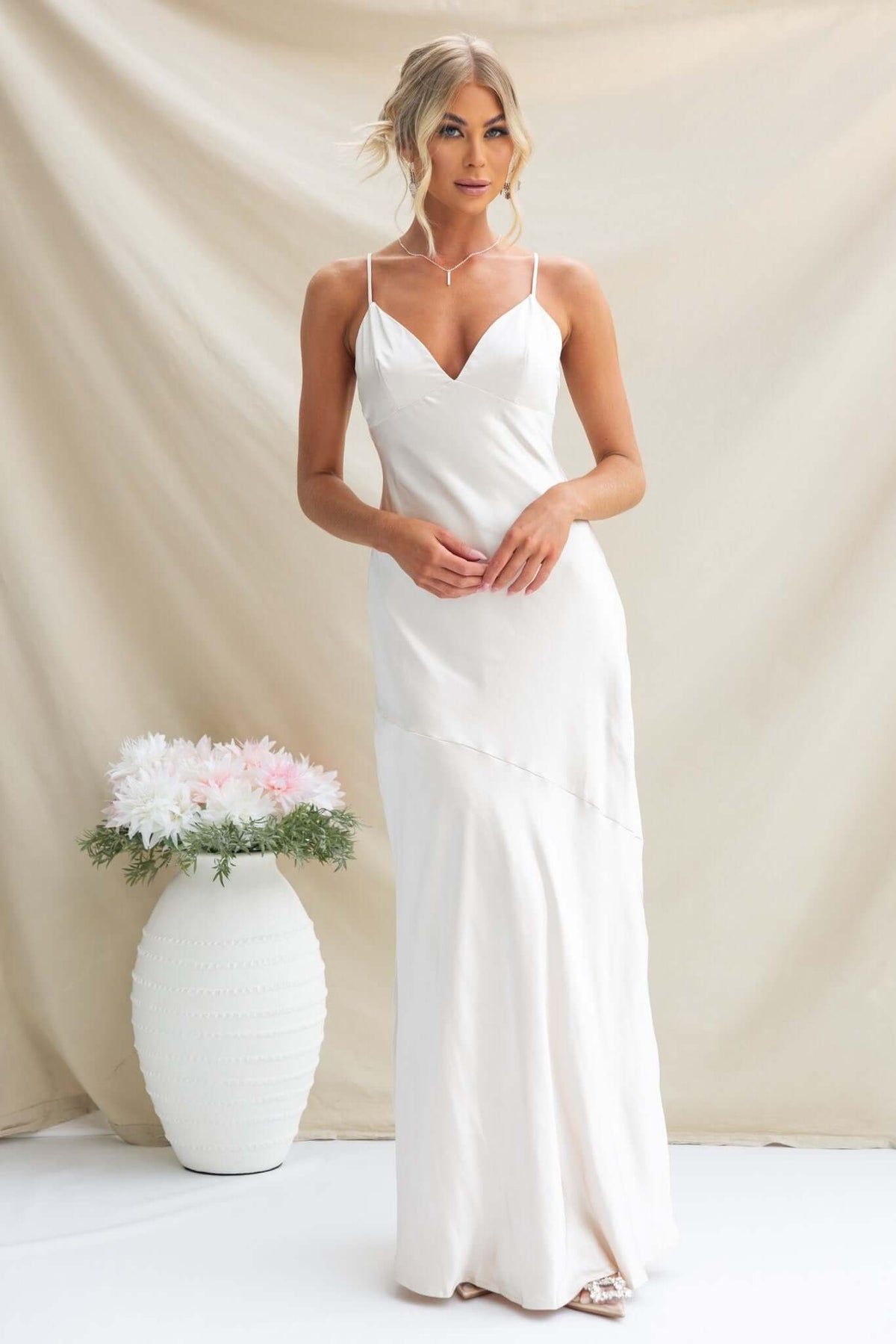 Elegant Coralina Maxi Dress in satin, featuring adjustable straps and a flattering fit, styled with a floral arrangement.