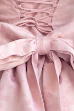 Close-up of a lace-up back detail with a large bow on a light pink strapless maxi dress.