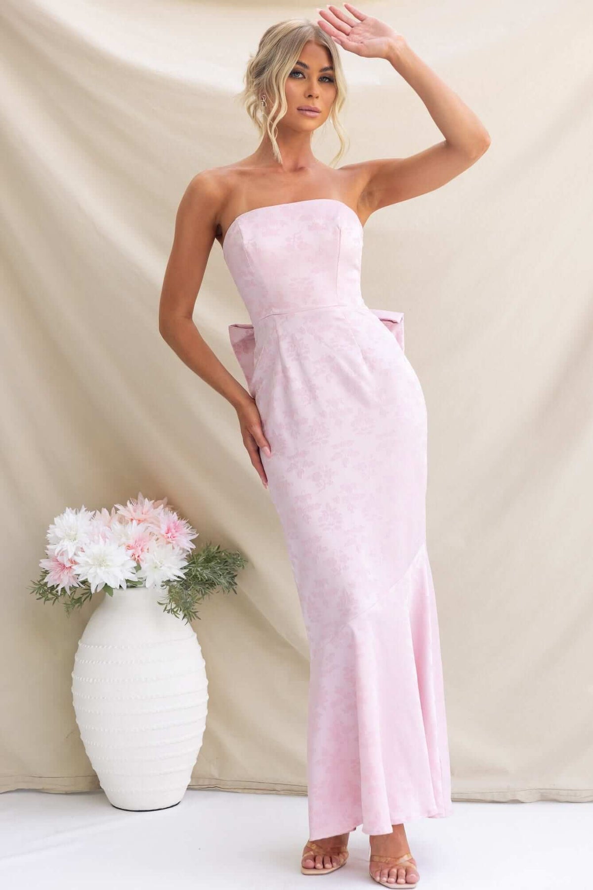 Model wearing a strapless pink Juanita Maxi Dress with a bow, styled elegantly against a soft background.