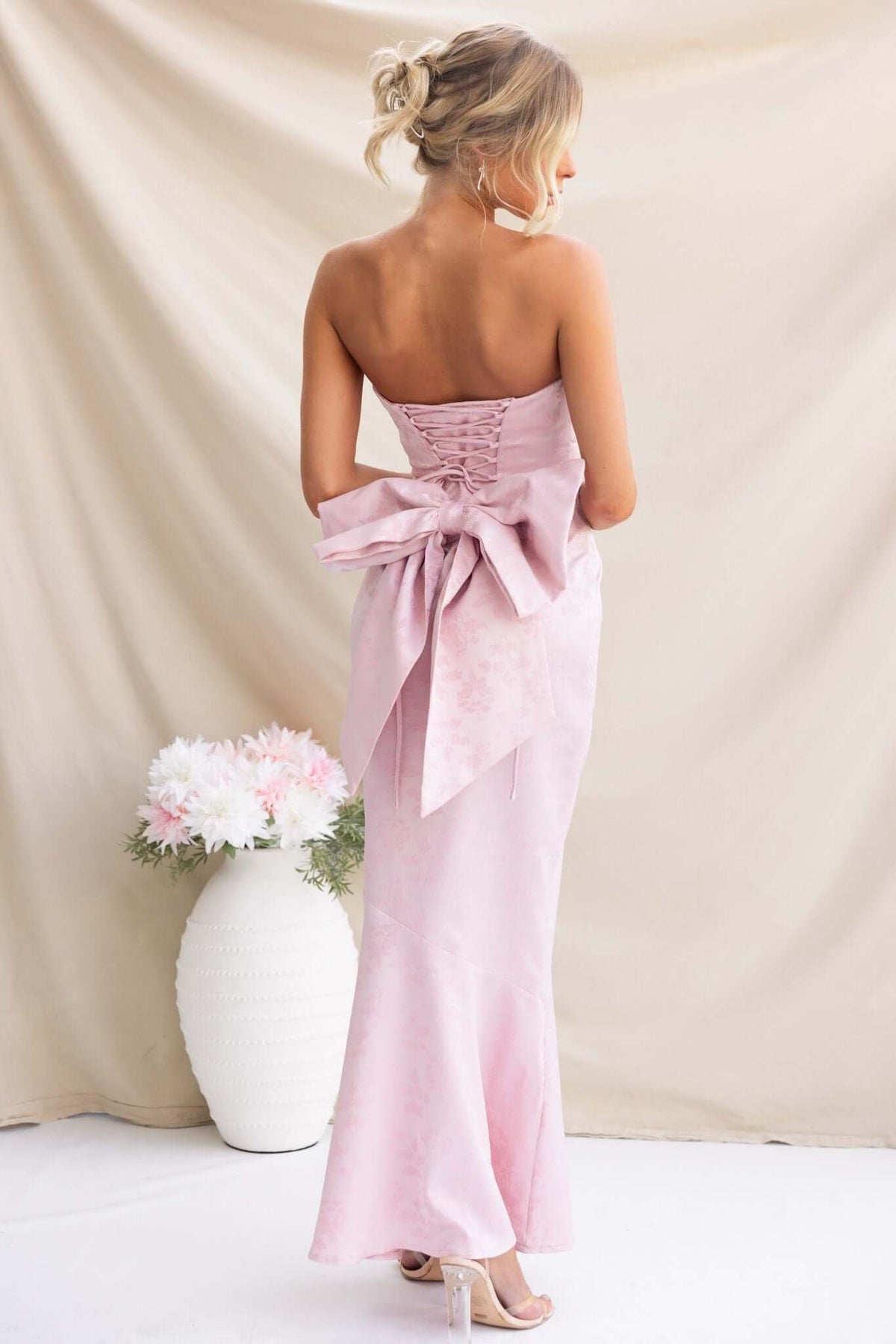 Back view of Juanita Maxi Dress in pale pink, featuring a strapless design, lace-up detail, and stylish bow.