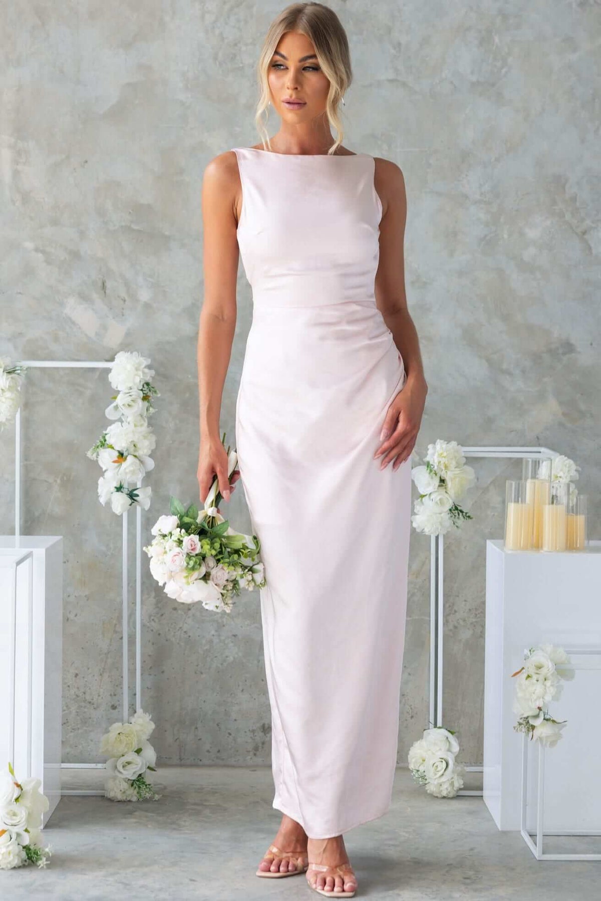 Model wearing Dakari Maxi Dress in blush satin, high neckline, perfect for bridal occasions, styled with a bouquet.