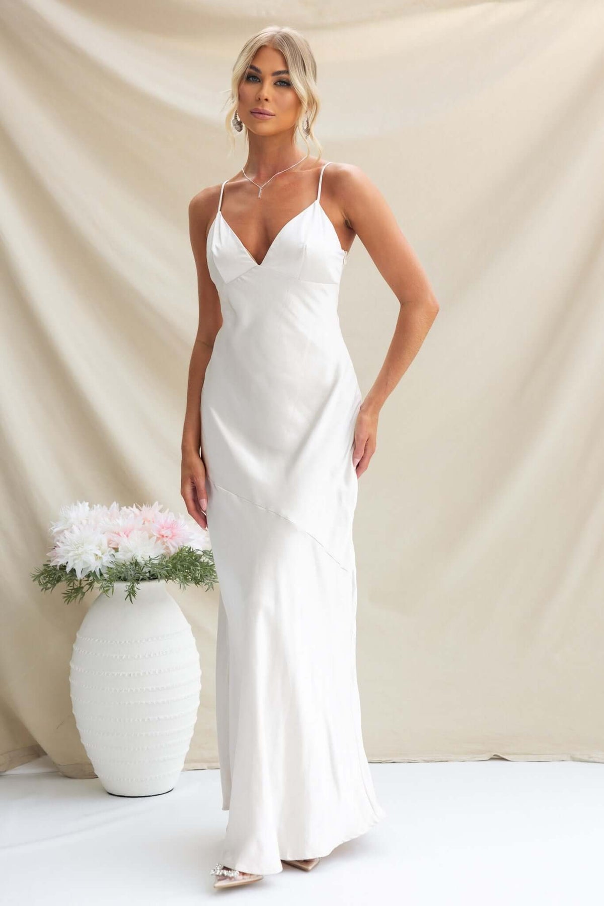 Elegant model wearing a satin coralina maxi dress with adjustable straps and side zip, styled with floral accents.
