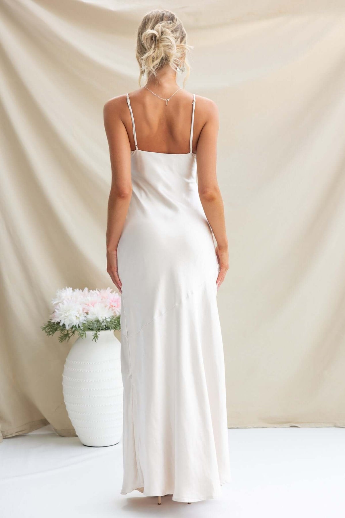 Back view of a woman in a satin Coralina Maxi Dress with adjustable straps against a neutral background.