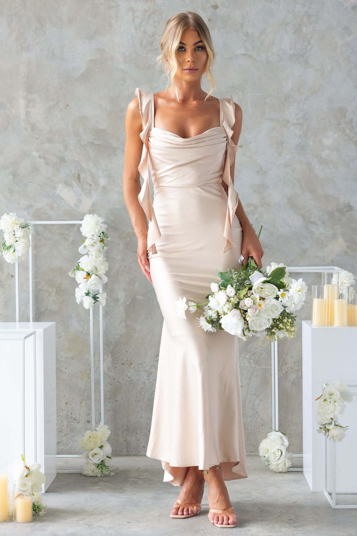 Ingrid Maxi Dress featuring adjustable straps, draping, and a fishtail hem, styled with floral bouquet.