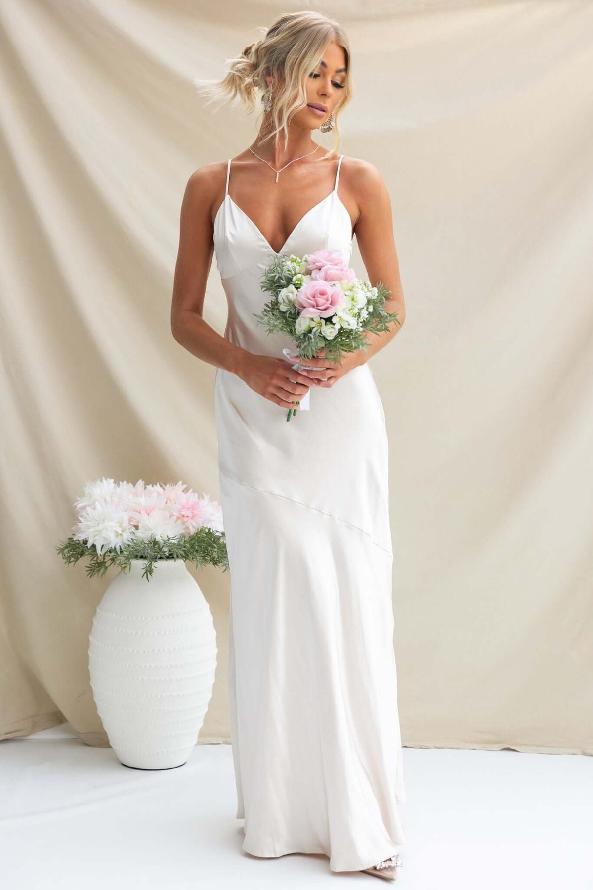 Model wearing a Coralina Maxi Dress, holding a bouquet of flowers, styled in a soft and elegant bridal setting.