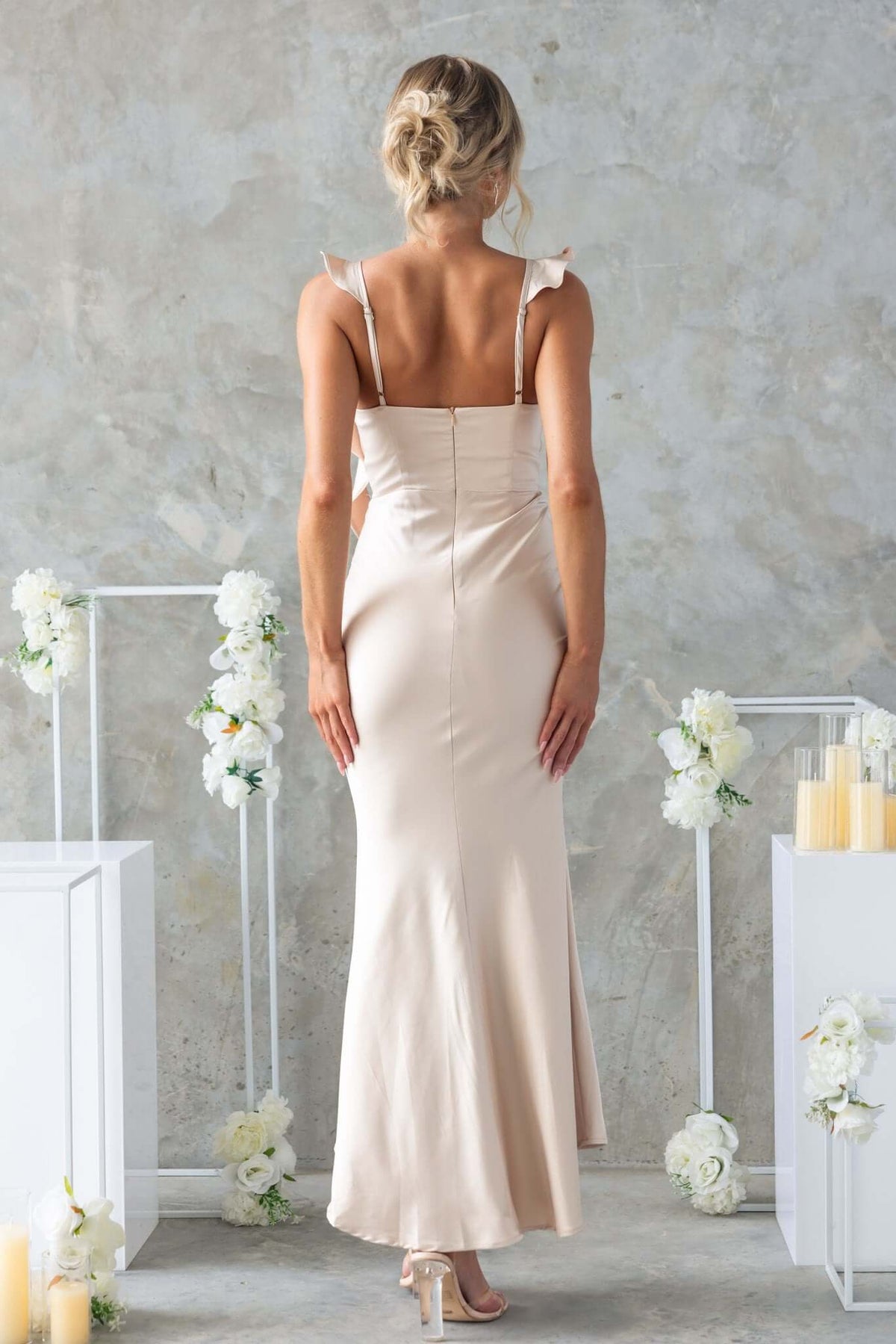 Back view of a woman in a beige Ingrid Maxi Dress with adjustable straps and subtle fishtail hem.