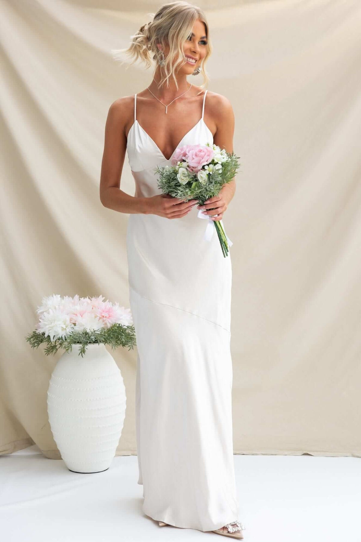 Chic model wearing the Coralina Maxi Dress, holding a bouquet, elegantly posed against a neutral backdrop.
