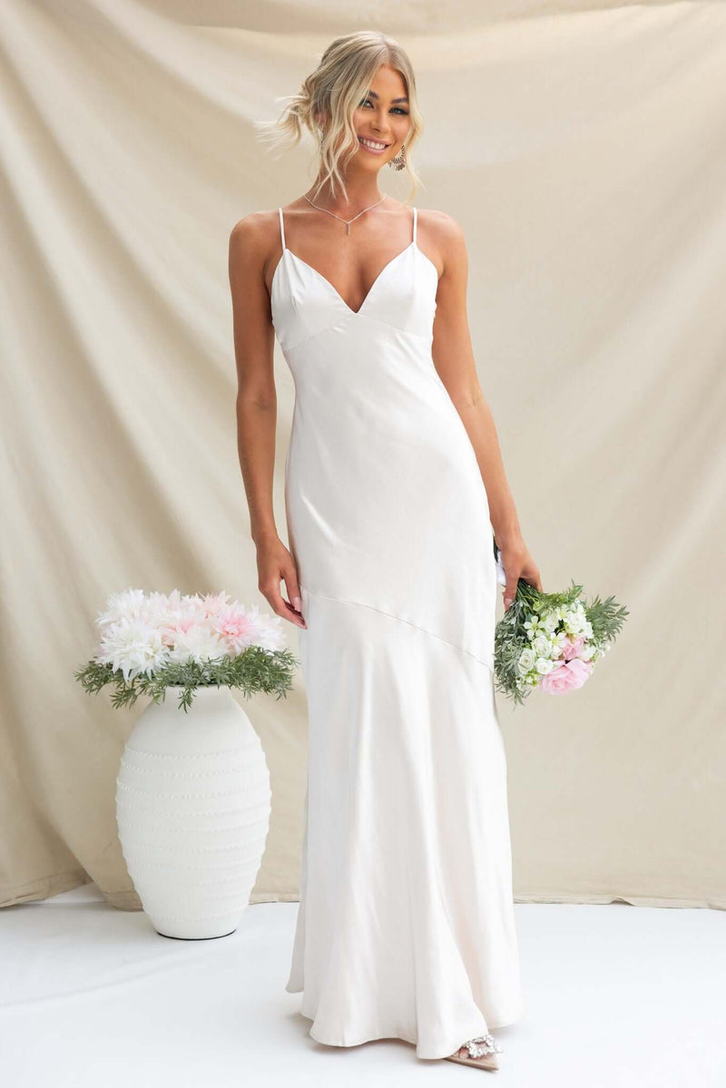 Model wears the Coralina Maxi Dress, featuring adjustable straps and satin fabric, holding a bouquet in a light setting.