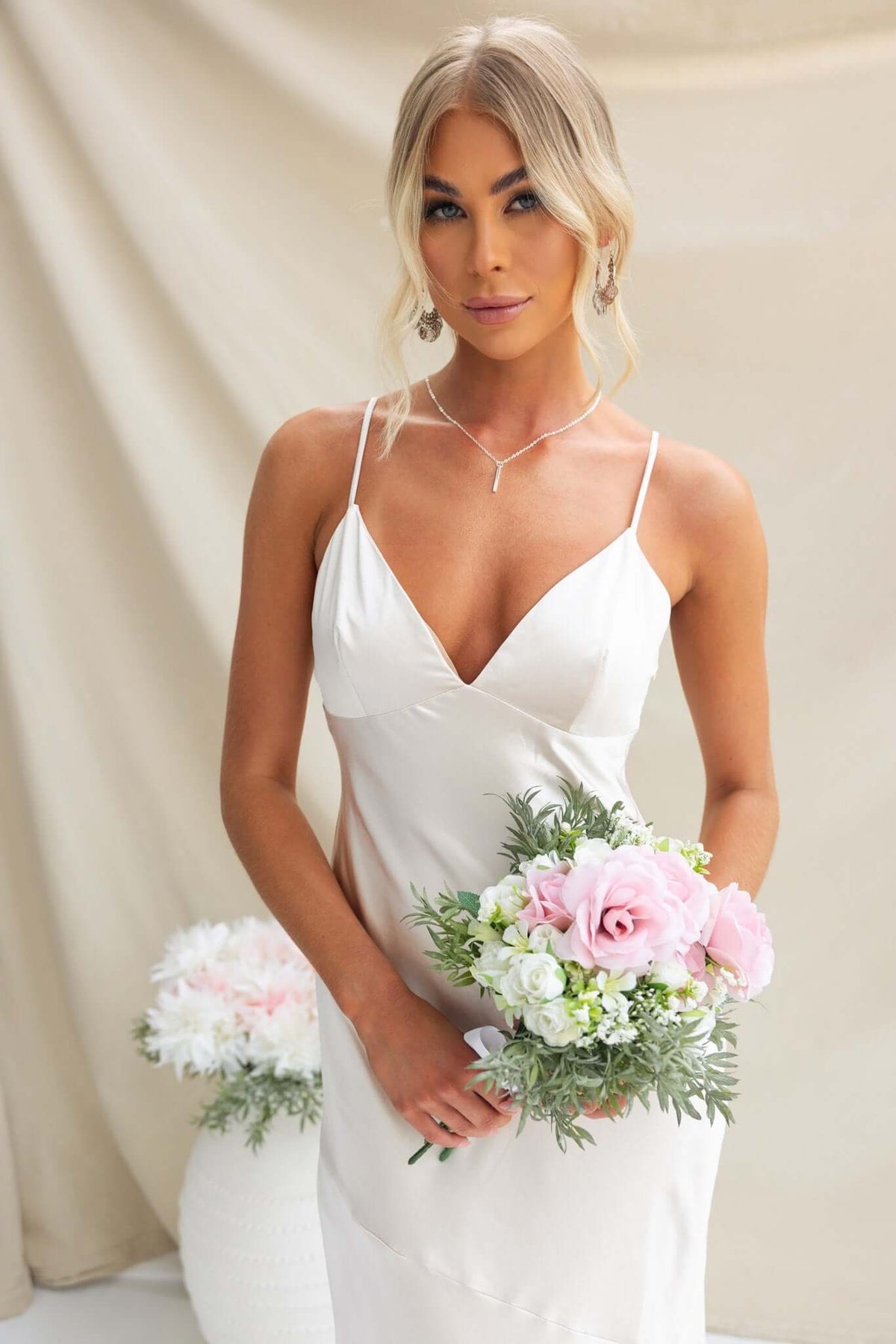 Model in a satin coralina maxi dress holding a bouquet of pink and white flowers, showcasing elegant bridal attire.