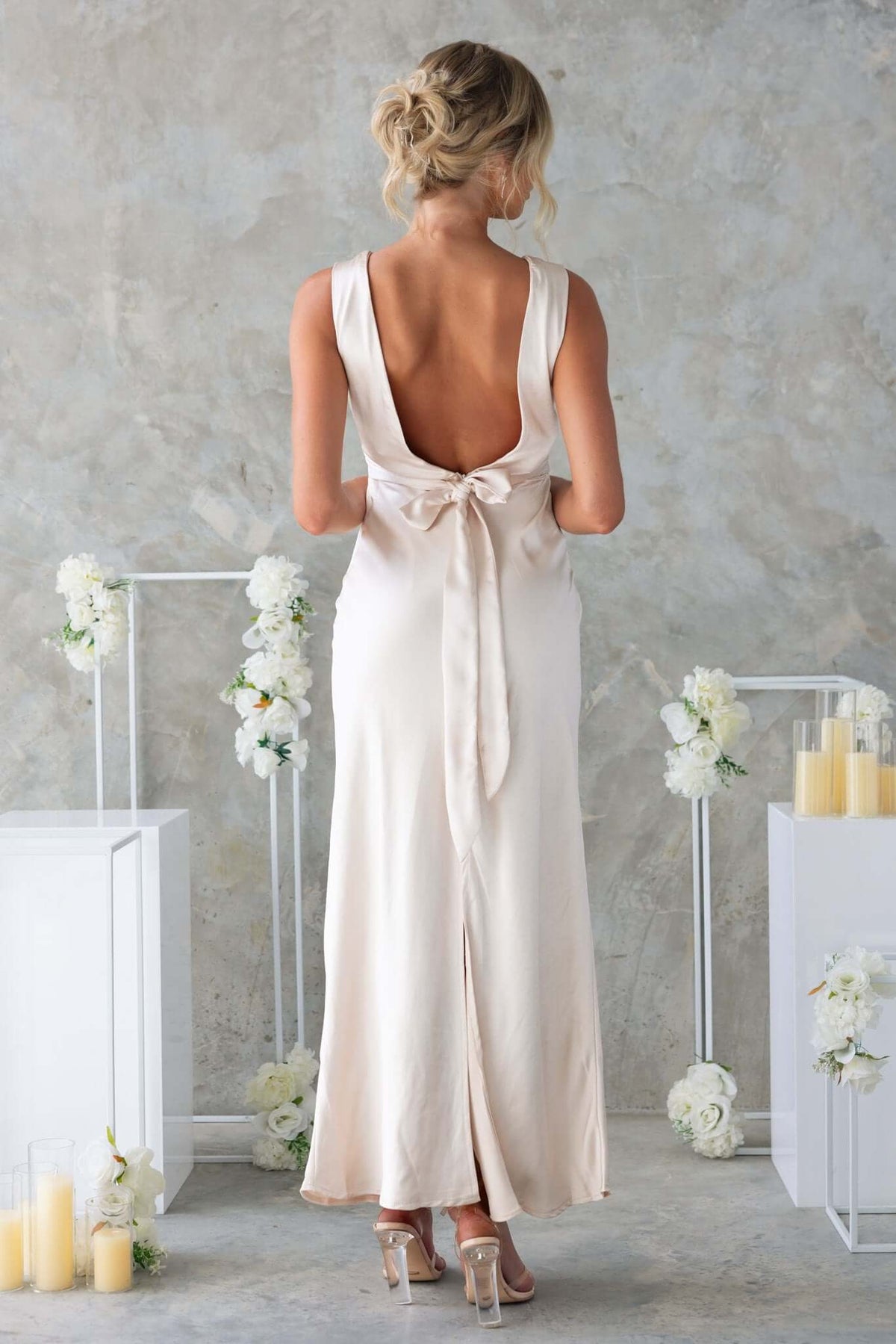 Back view of Alika Maxi Dress in satin, showcasing V-neckline, tied bow, and elegant split design.