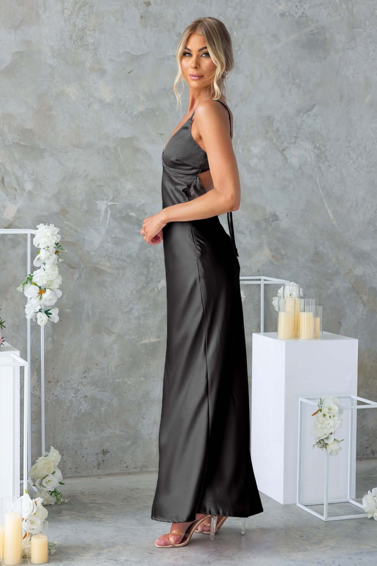 Hasina Maxi Dress in black satin with V-neckline and adjustable straps, styled against a modern backdrop.