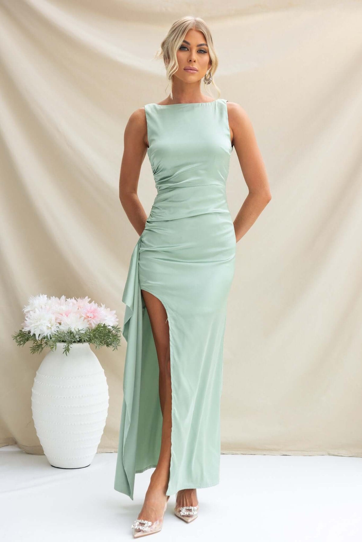 Kenzie Maxi Dress in mint green featuring high neckline, side split, and ruffle, styled with elegant heels.