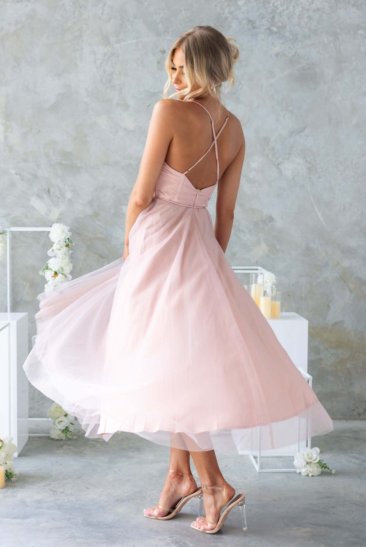 Back view of a model wearing a blush pink Florence Midi Dress with adjustable straps and flowing tulle skirt.