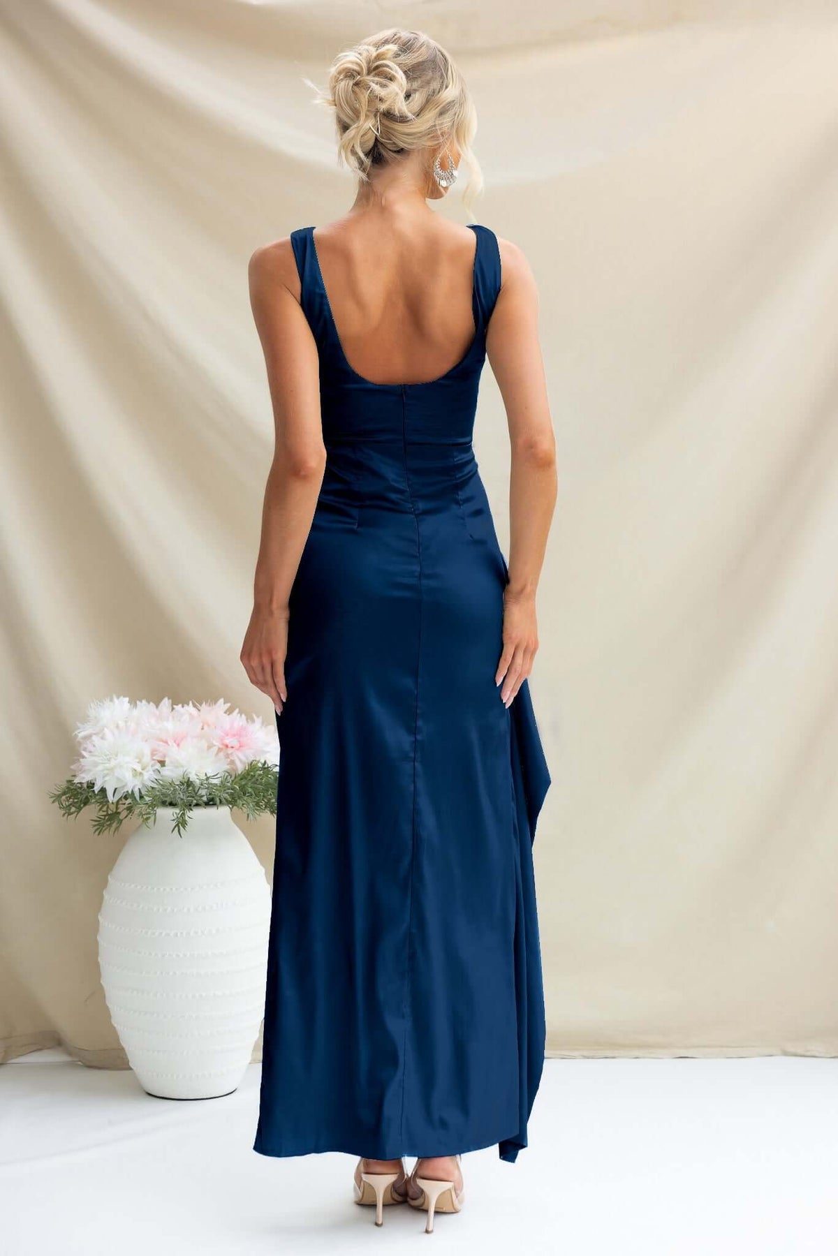 Model showcasing the back view of the Kenzie Maxi Dress in navy, featuring a high neckline and elegant satin fabric.