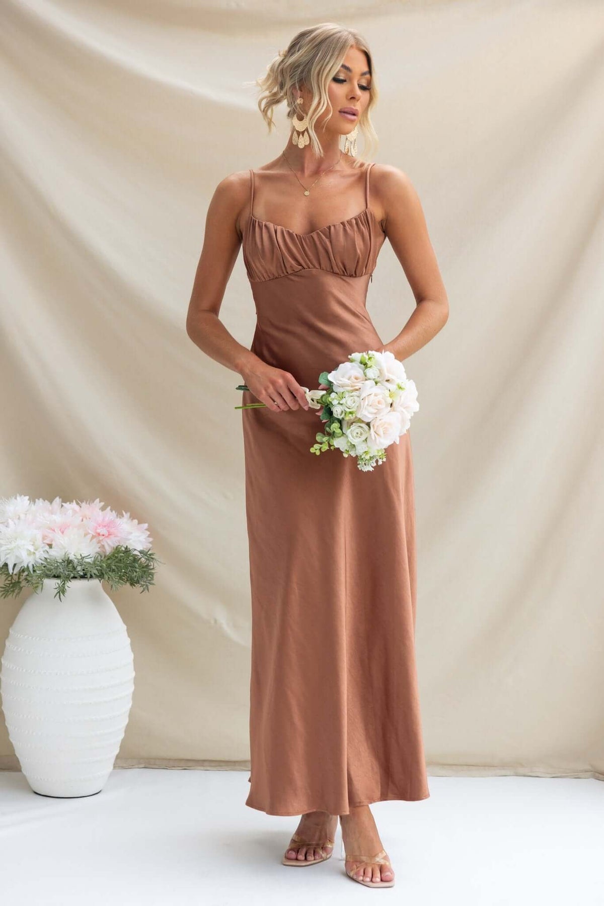 Maeya Maxi Dress in brown, featuring adjustable straps and gathered bust, styled with a floral bouquet.