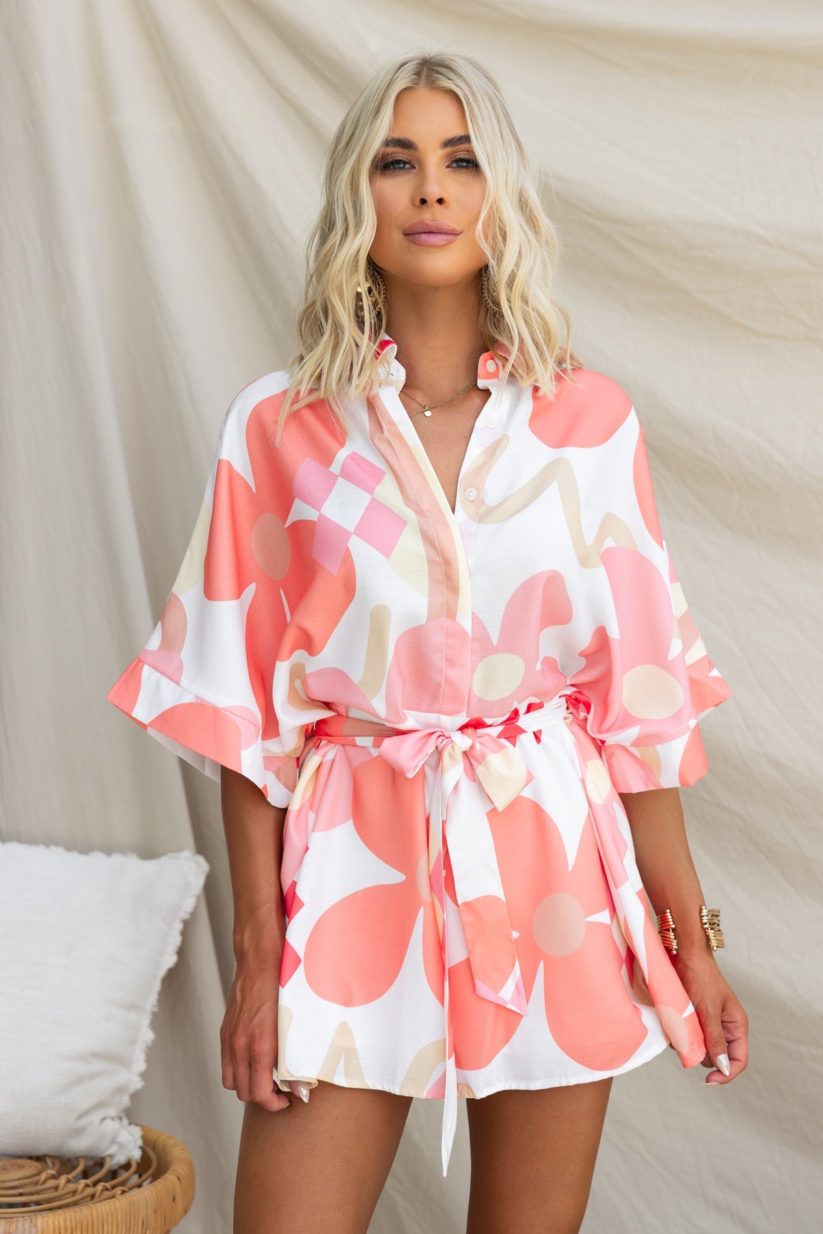 Model wearing a pink abstract print Sundown Playsuit with a collar and button-up front, tied at the waist.