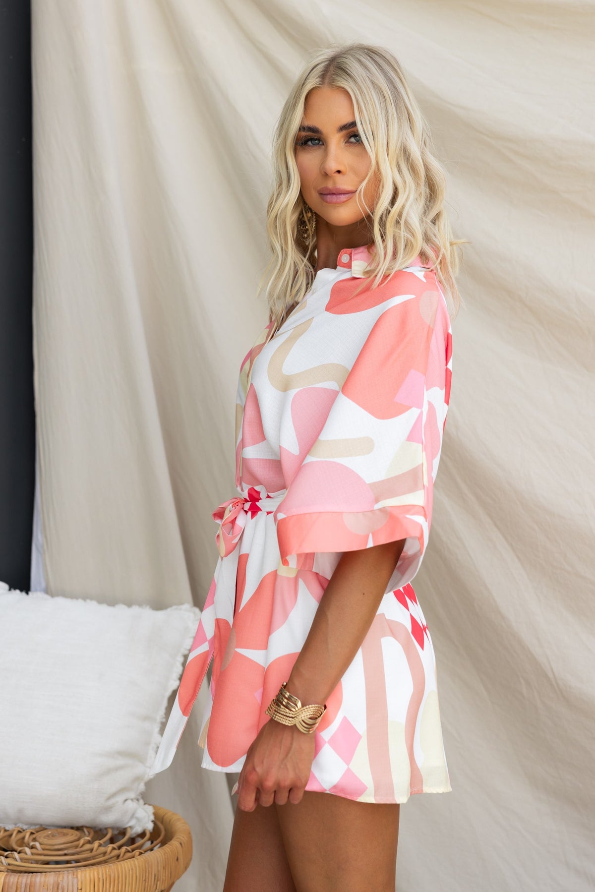 Model wearing a pink abstract print sundown playsuit with a collar, featuring a removable fabric tie.