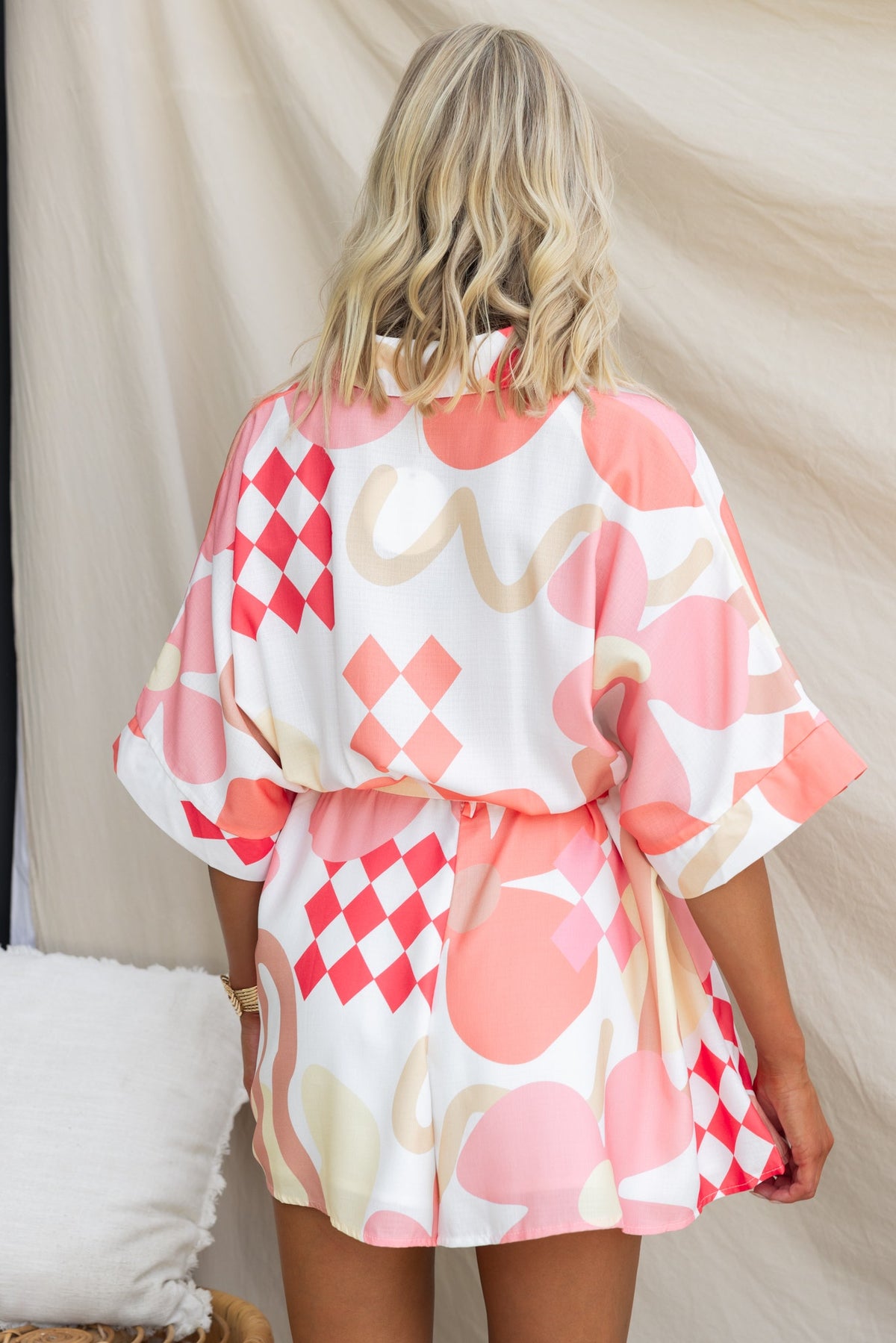 Back view of a model wearing a colorful abstract print Sundown Playsuit with oversized fit and fabric tie.
