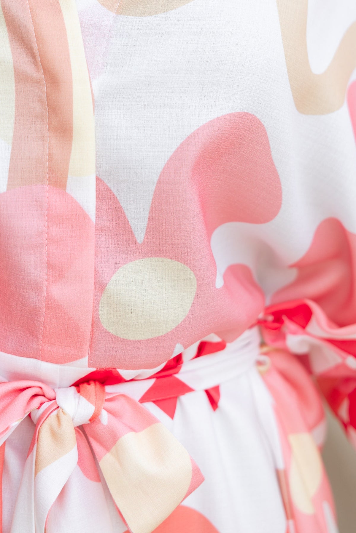 Close-up of the Sundown Playsuit with abstract pink and beige print, featuring a removable tie at the waist.