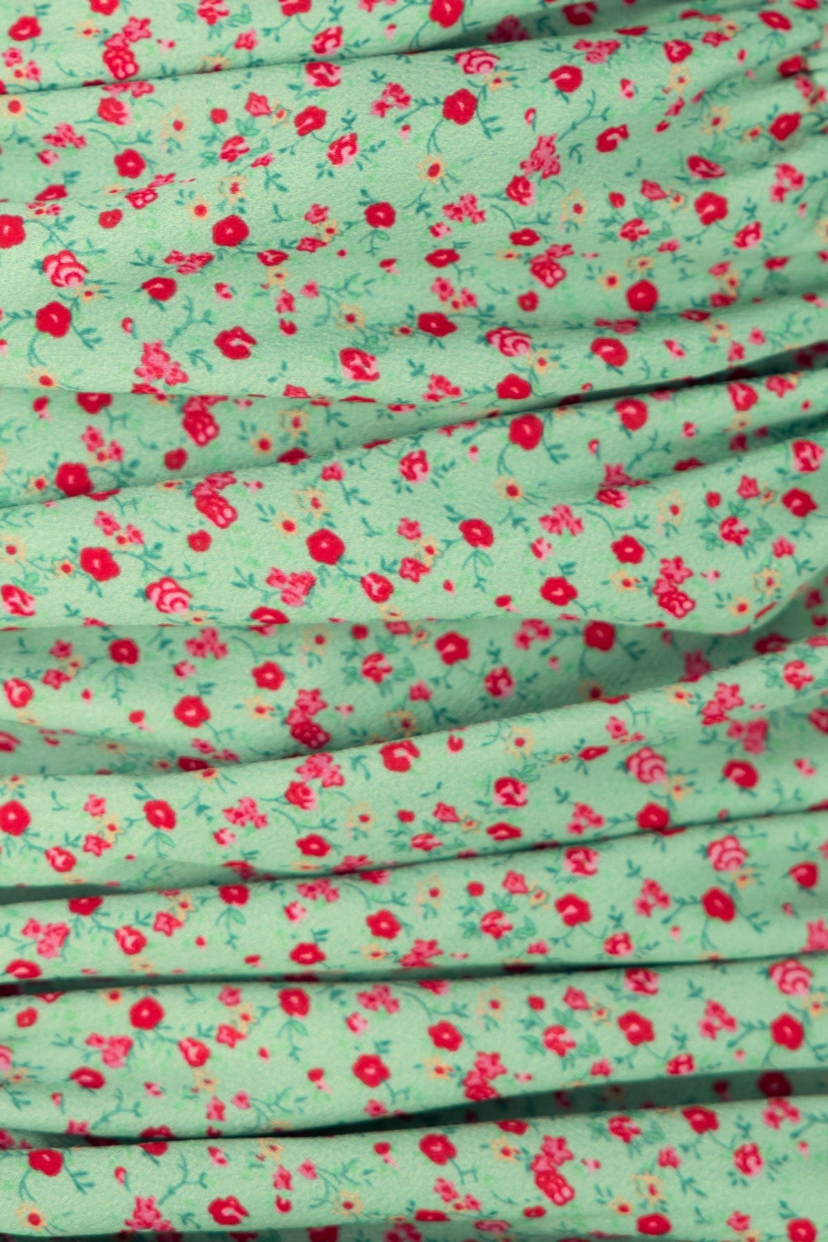 Close-up of the Ikaria Dress floral fabric featuring green background and red flowers, showcasing ruching detail.