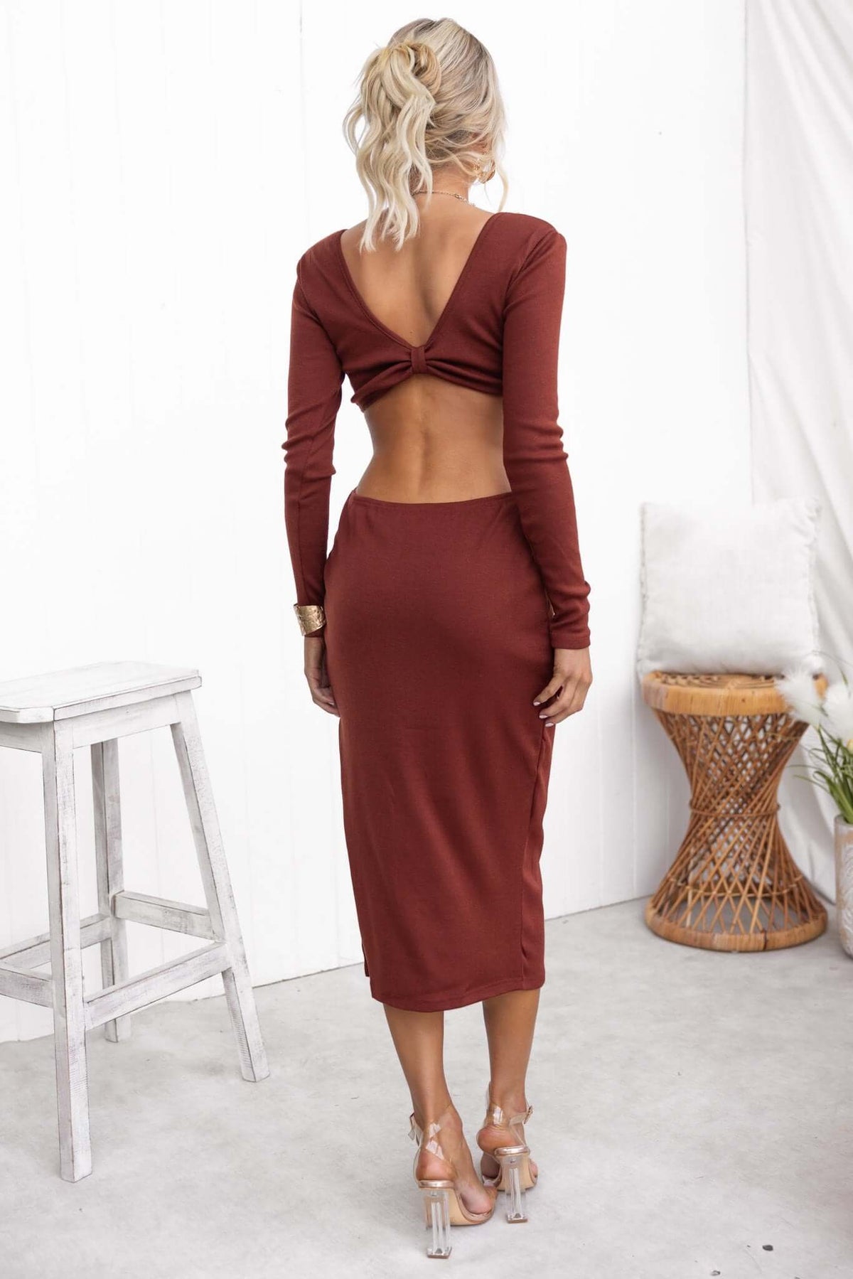 Back view of a woman wearing a rust-colored Kartier midi dress with cut-out waist and long sleeves.