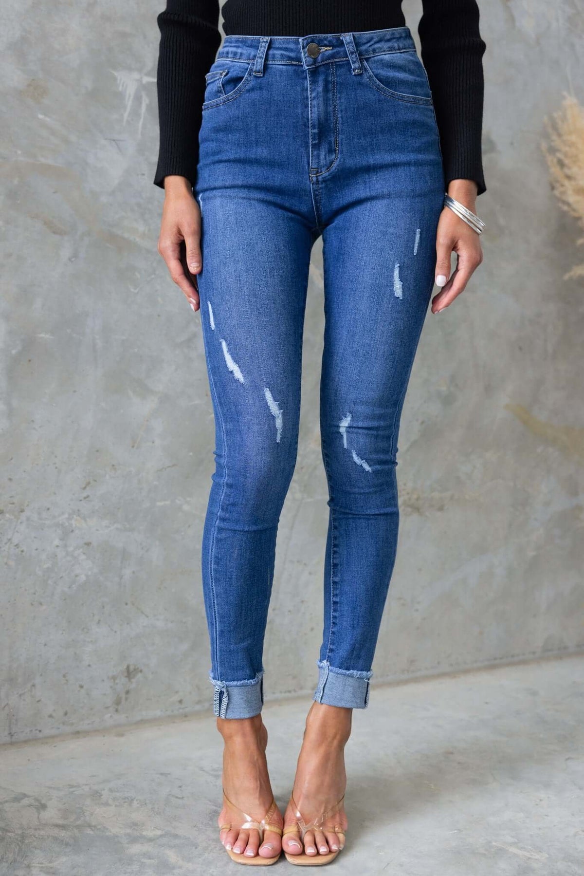 Mid-high waist distressed denim jeans with pockets, featuring a stretchy fit and rolled cuffs for a stylish look.