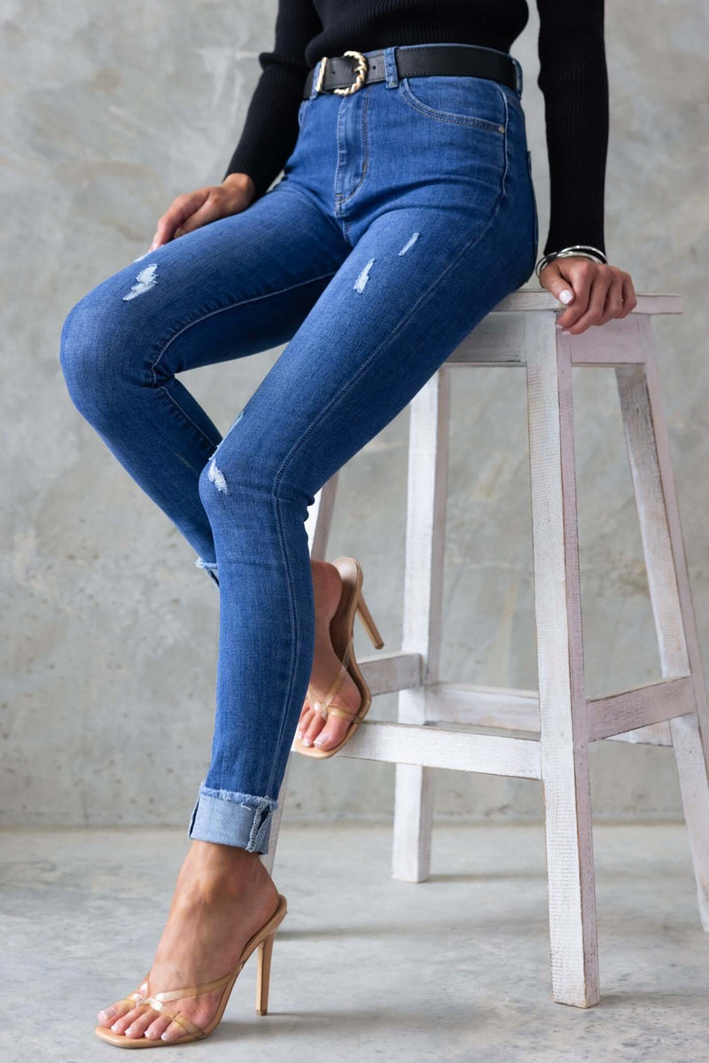 Lettie Jeans: distressed mid-high waist denim jeans with pockets, styled with heels and a belt.