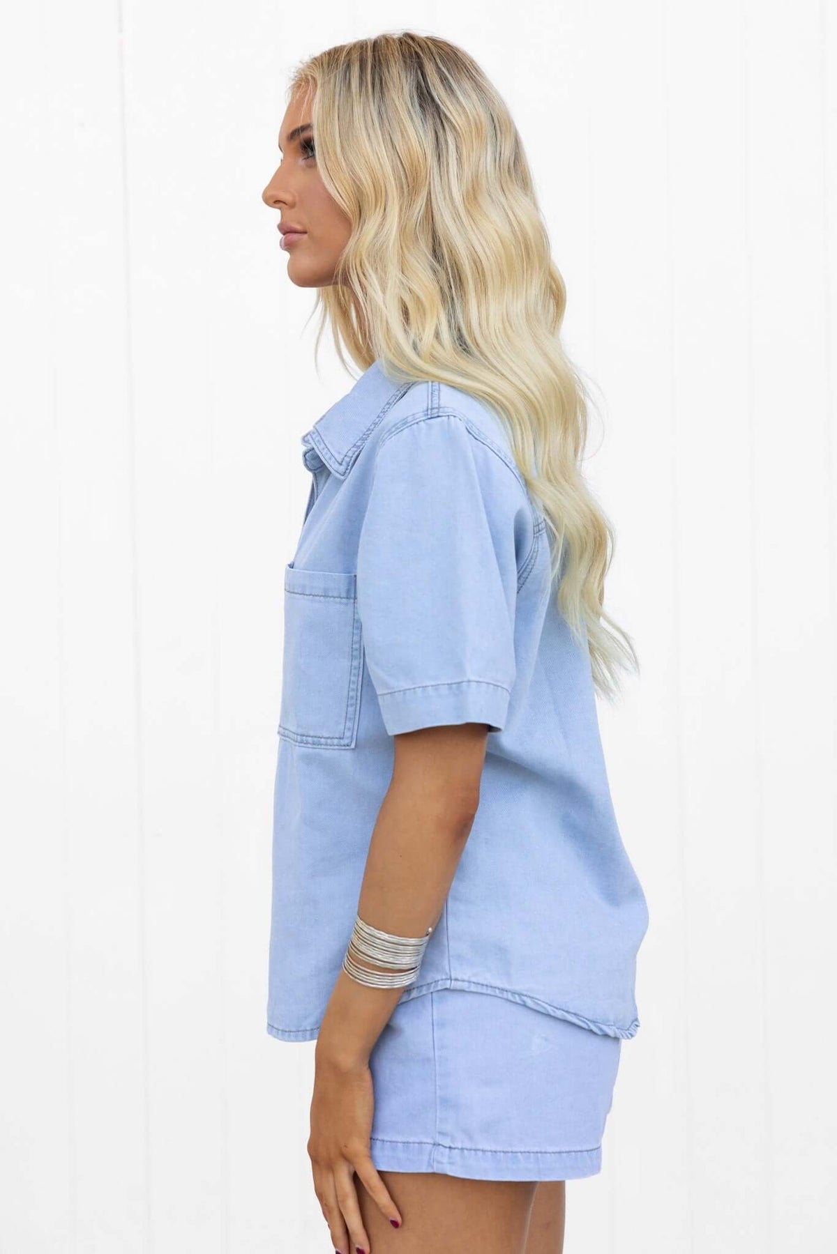 Side view of a woman wearing a light blue chambray Winslow shirt with a pocket, showcasing a casual summer style.