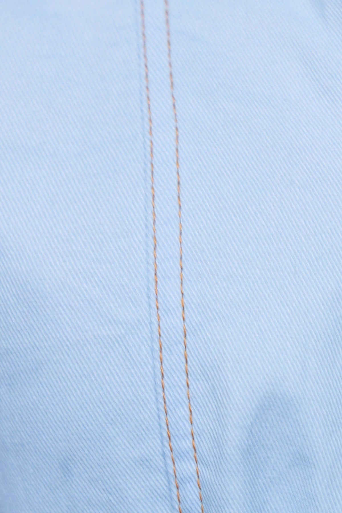 Close-up of light blue denim fabric with visible stitching details showcasing texture and quality.
