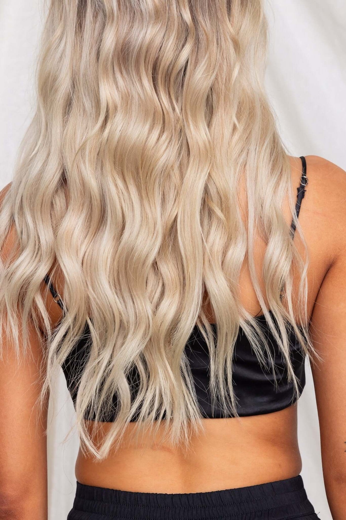 Back view of a model wearing a black satin Under Control Top with adjustable straps, showcasing long, wavy blonde hair.