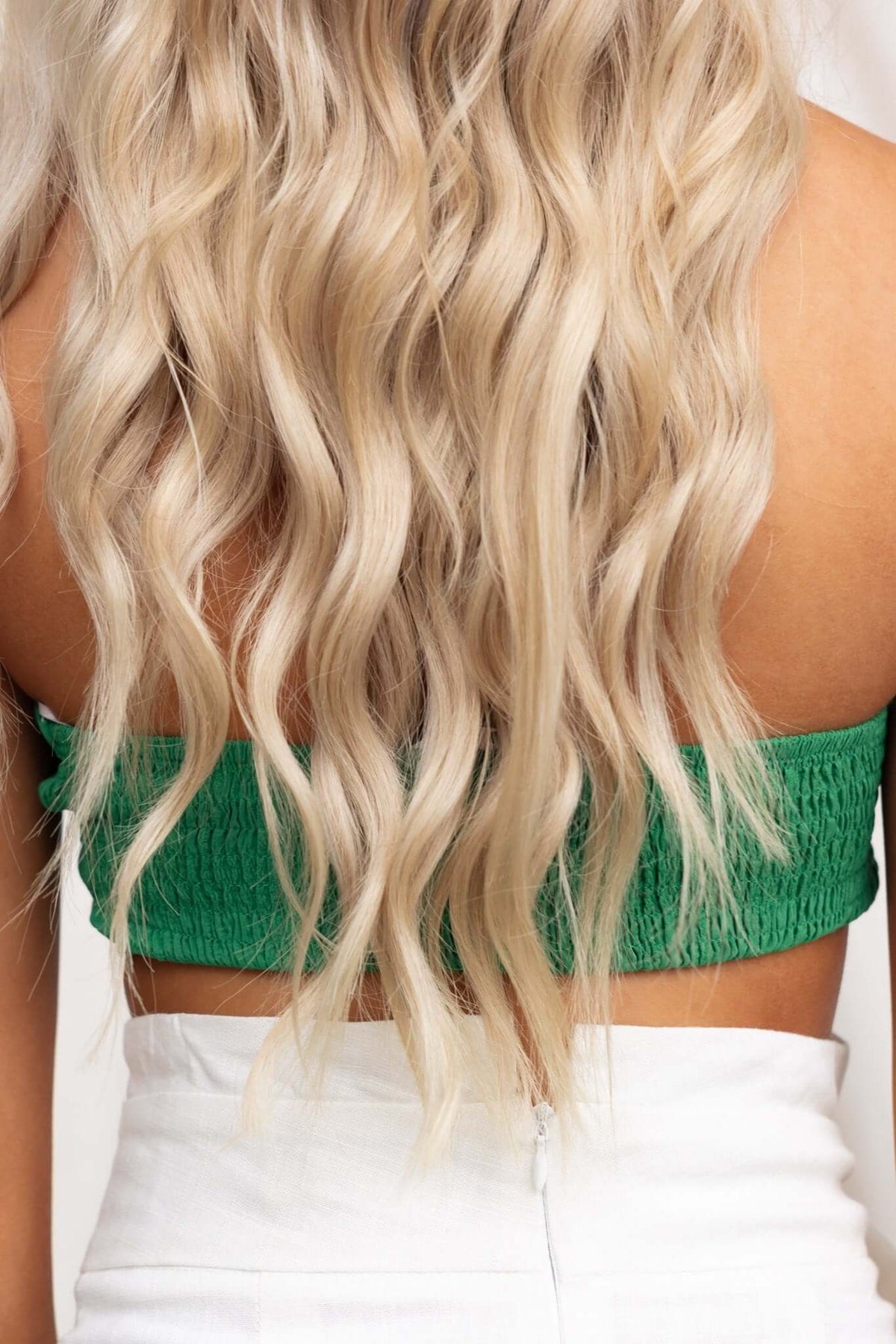 Back view of a woman wearing a textured green Omalie Top with wavy blonde hair, showcasing the semi-sheer design.