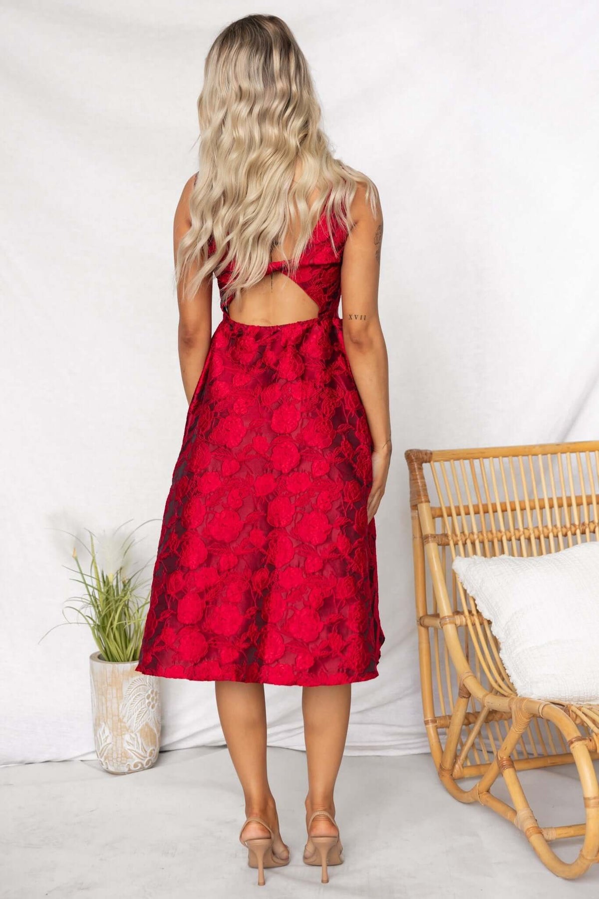 Back view of a woman in a red textured midi dress with an open back, styled with light brown heels.
