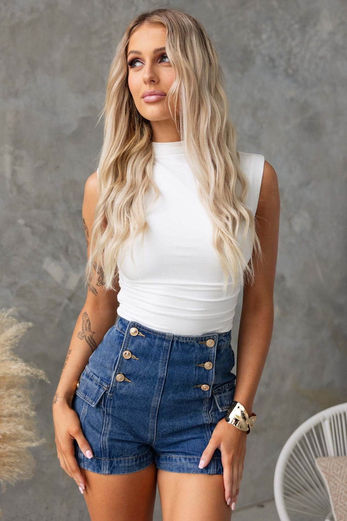 Model showcasing Osment Denim Shorts with a mid-high waist, button-up front, and side pockets, styled with a white top.