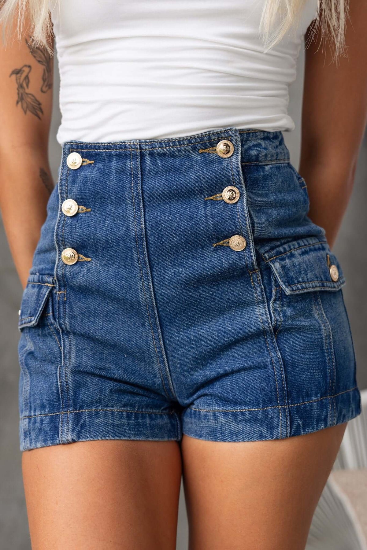 Osment Denim Shorts featuring a mid-high waist, button-up front, and side pockets, stylishly worn by a model.