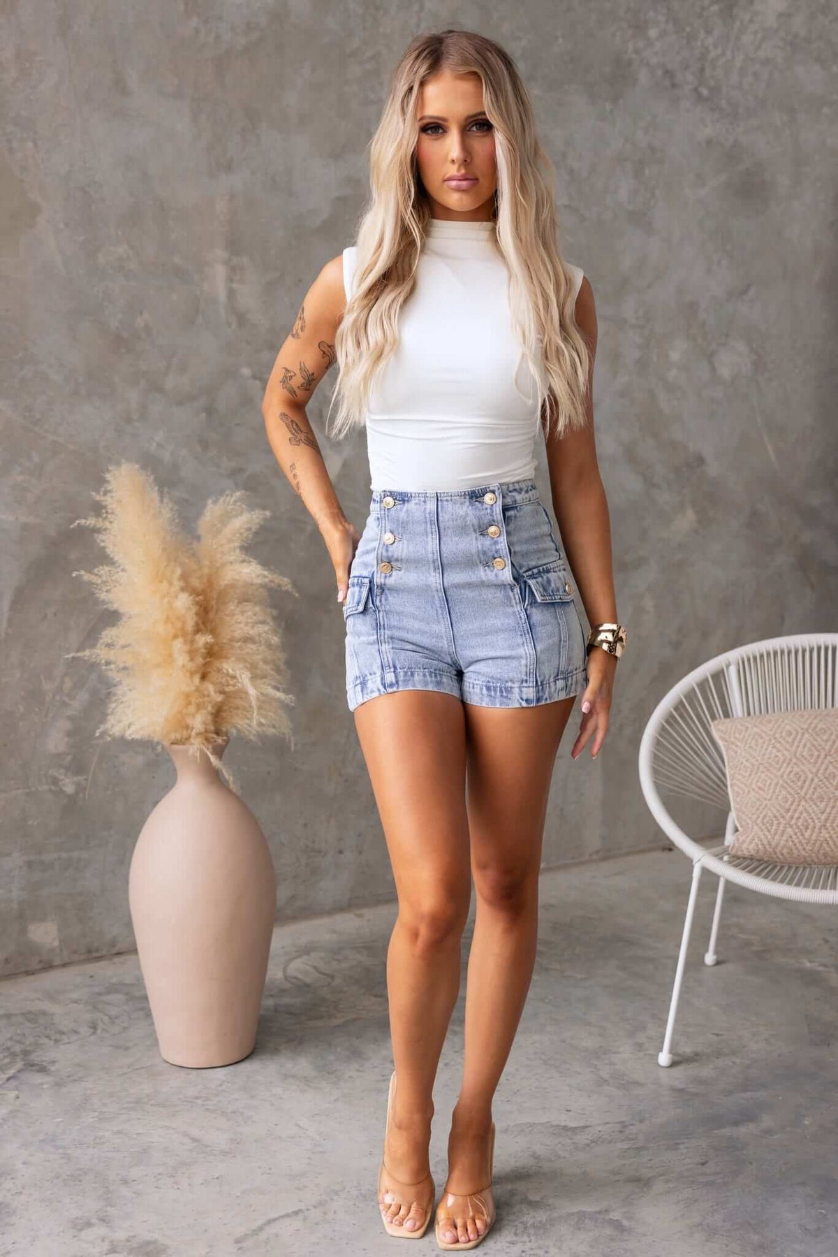 Model wearing Osment Denim Shorts, featuring a mid-high waist and button-up front, styled with a white tank top.