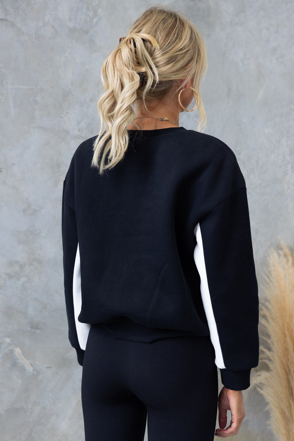 Back view of a black Roma Jumper with white side stripes, featuring a relaxed fit and ribbed cuffs.