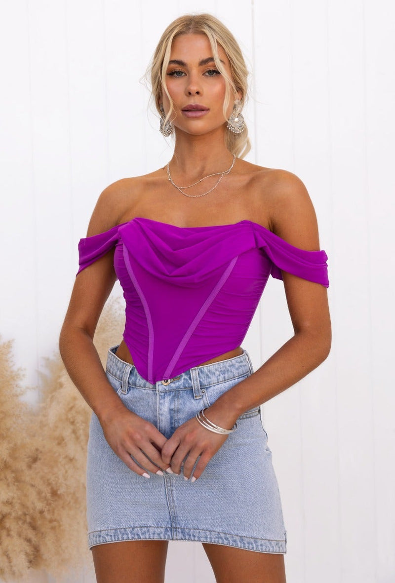 Taria Top: Off-shoulder corset top in vibrant purple with structured boning and zip back, styled with a denim skirt.