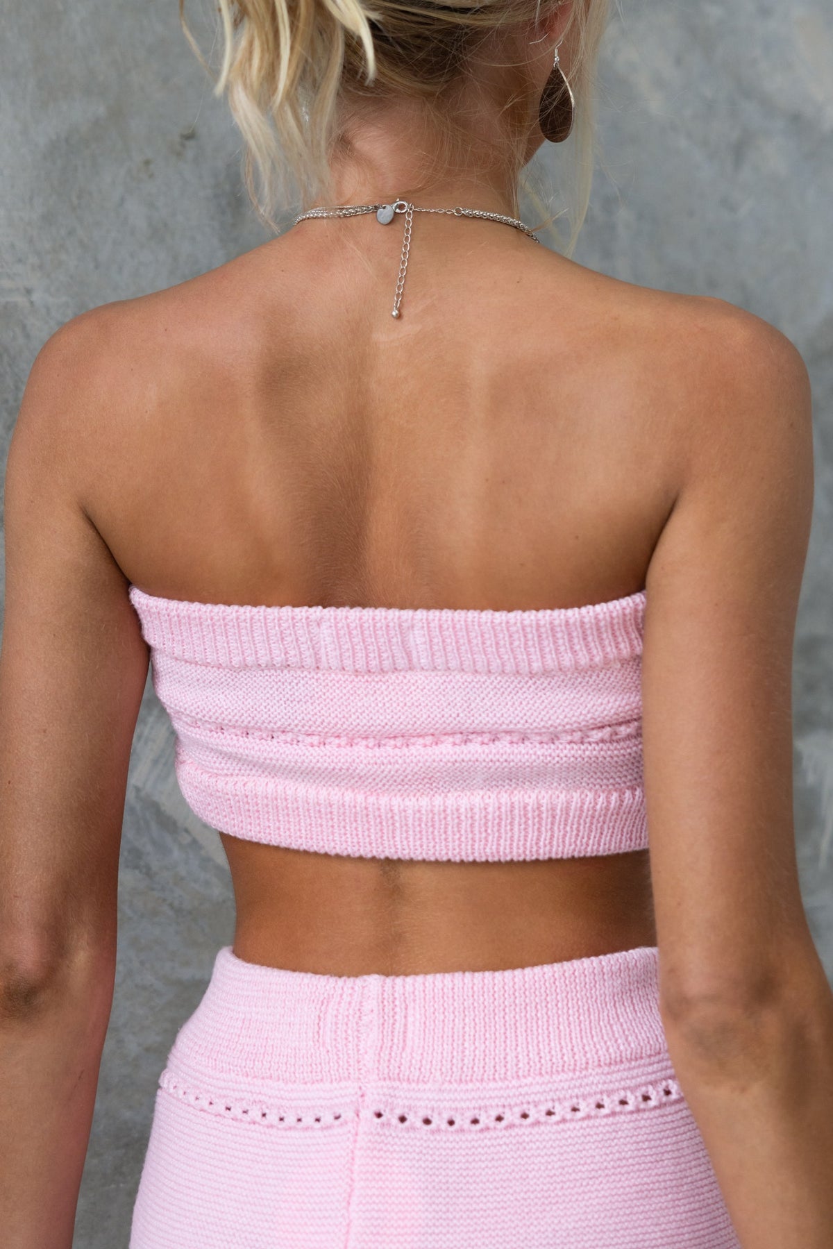 Back view of a model wearing a pink strapless knit Pearla Top with ring detail, showcasing a semi open weave design.