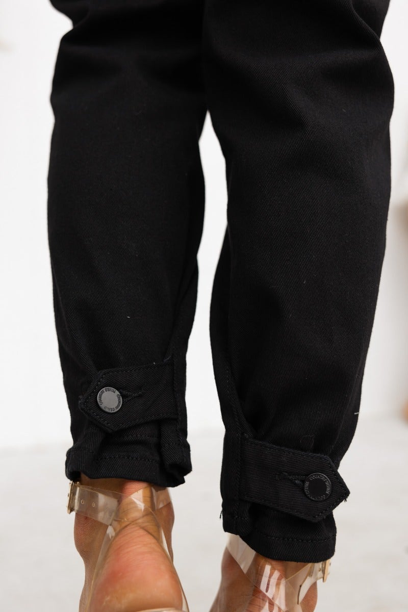 Close-up of black denim jeans with button cuff ankles and clear shoes, showcasing mid-high waist fit.