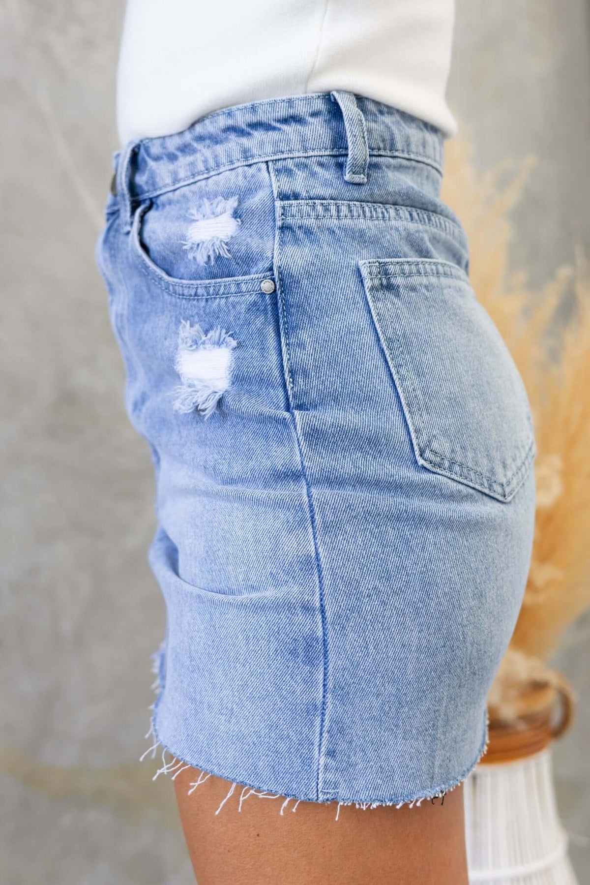 Dusty Road Denim Skirt featuring distressed details, raw hemline, and pockets in light blue wash.