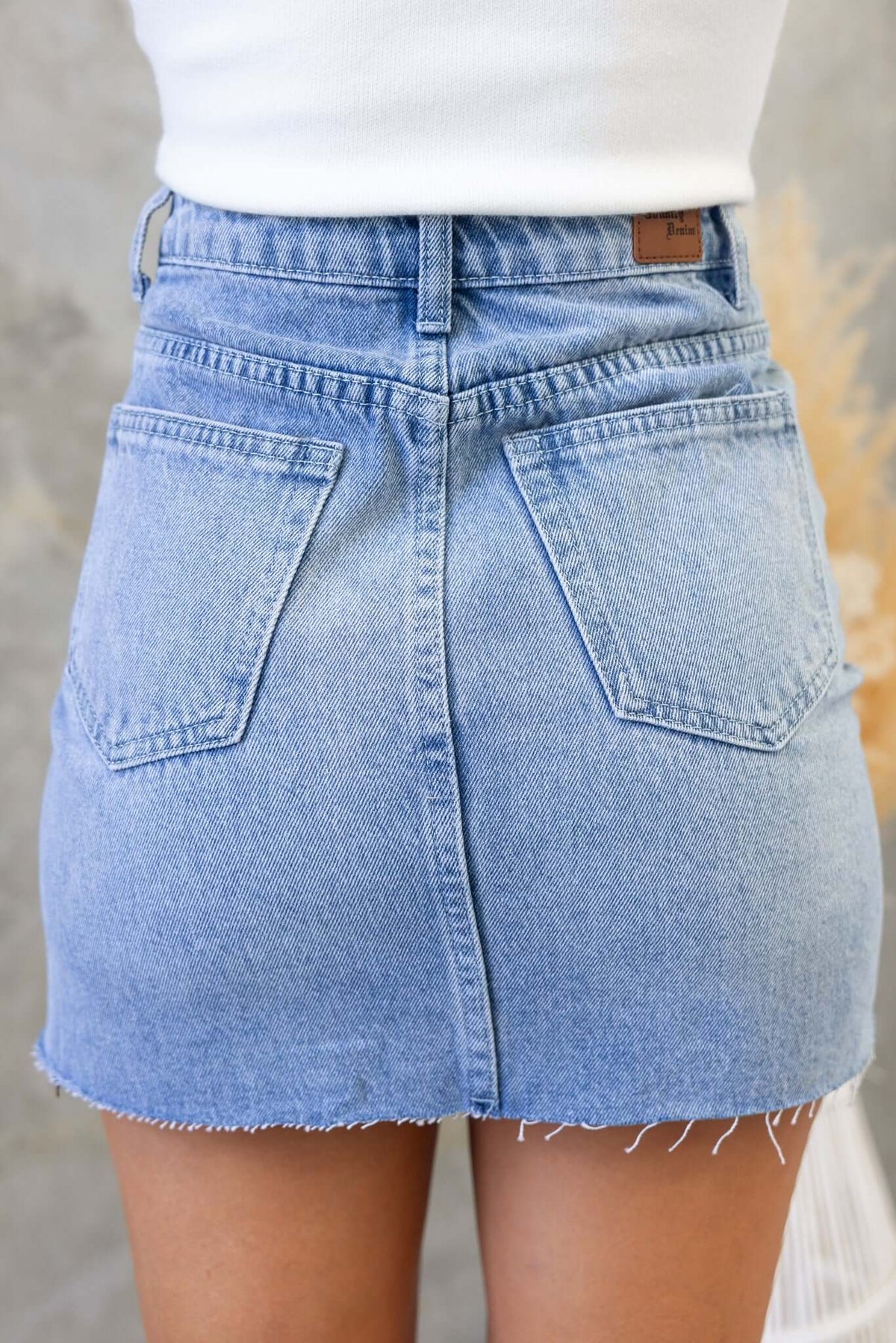 Back view of a Dusty Road Denim Skirt, featuring distressed details, raw hemline, and two pockets.
