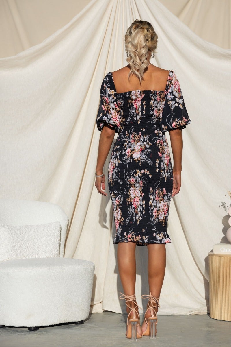 Back view of Arabella Midi Dress featuring floral design, elastic sleeves, and fitted silhouette, styled with strappy heels.