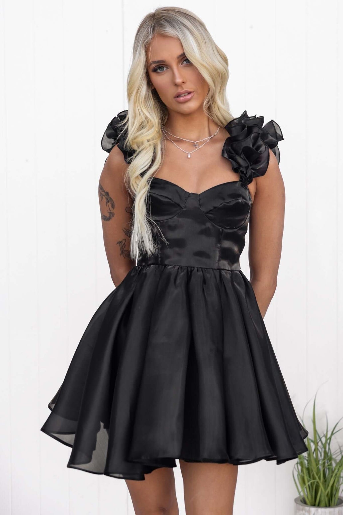 Model wearing the Ermia Dress, a black chiffon dress with ruffle straps and a fitted bodice, showcasing a flattering silhouette.