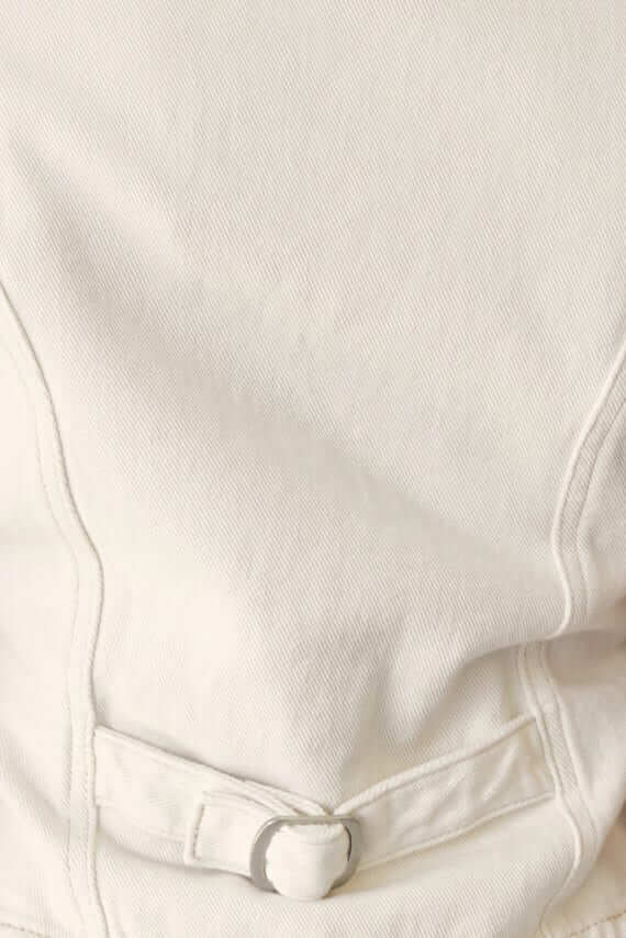 Close-up of fabric detail showing a button and stitching on white denim.