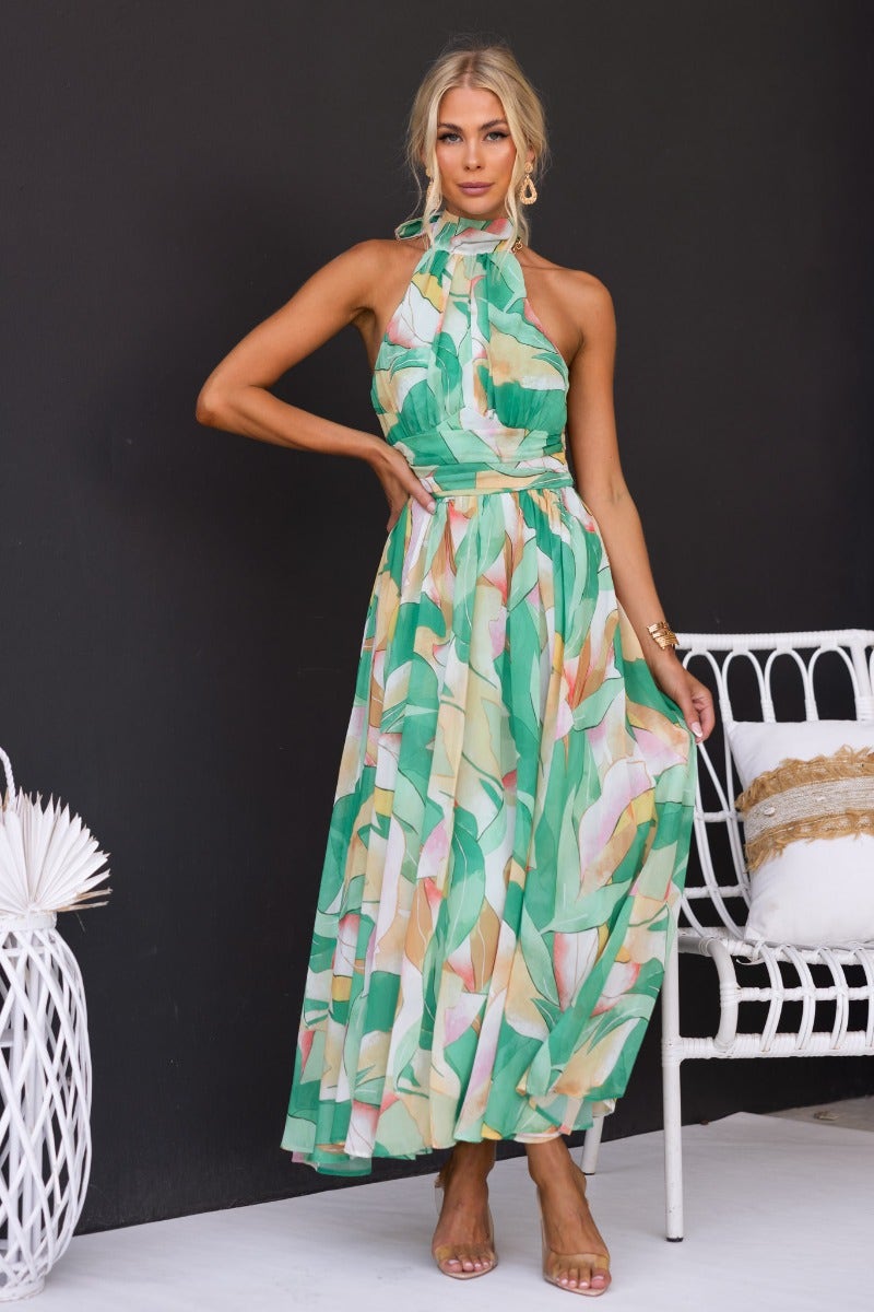 Model wearing a floral print Little Things maxi dress with a high tie neckline and flowing skirt.