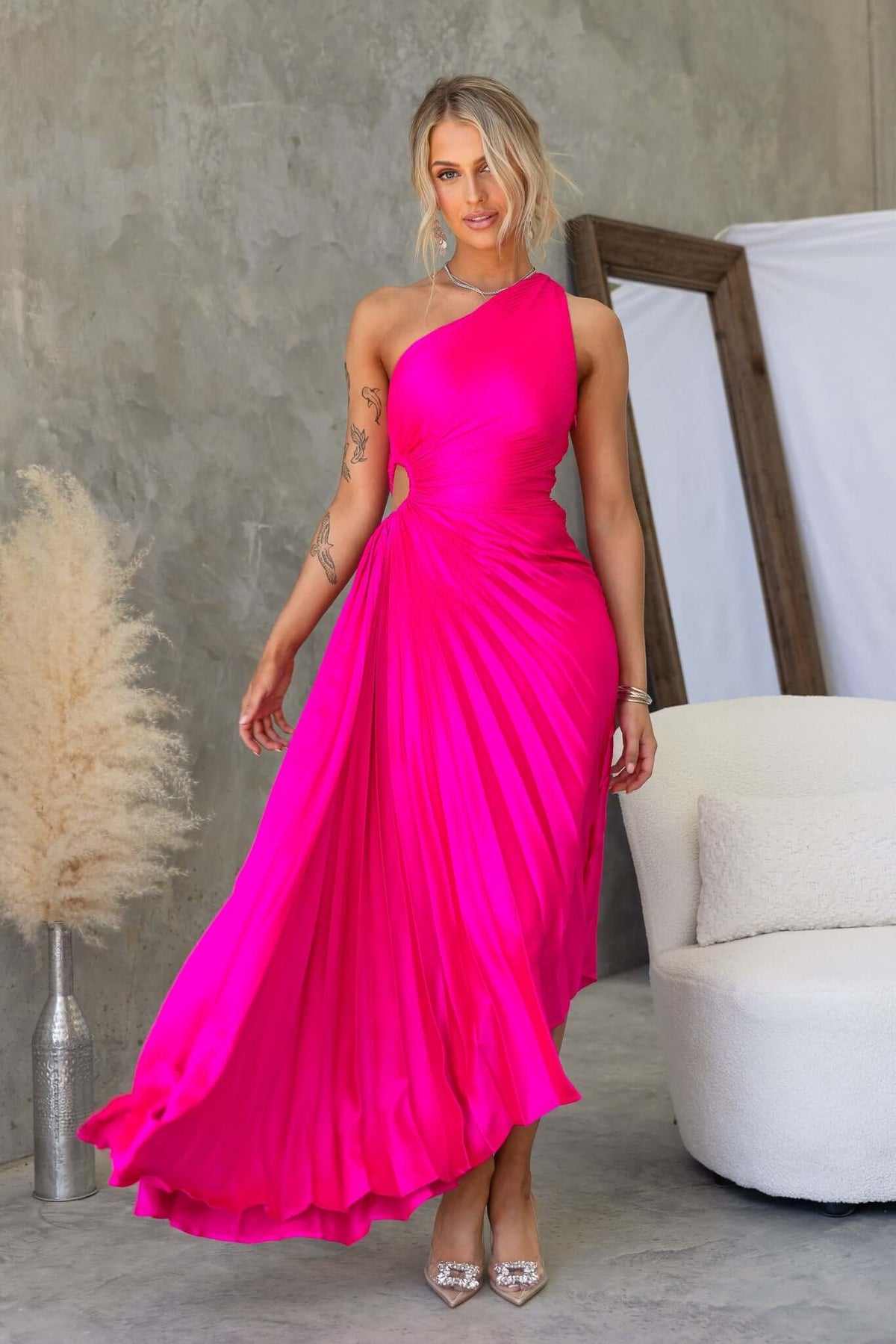 Model wearing a vibrant pink Olympia Maxi Dress with a one-shoulder neckline and cut-out waist, showcasing accordion pleats.