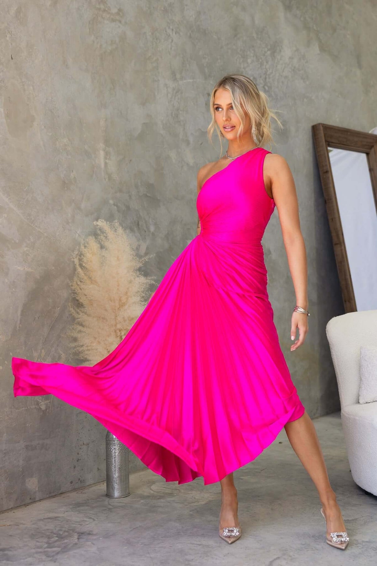 Model in a vibrant pink Olympia Maxi Dress with one-shoulder design and pleated skirt, showcasing elegant style.