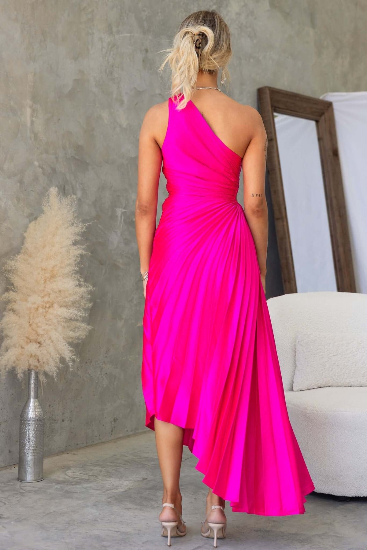 Back view of a vibrant pink one-shoulder maxi dress with pleated design, showcasing elegance and modern style.